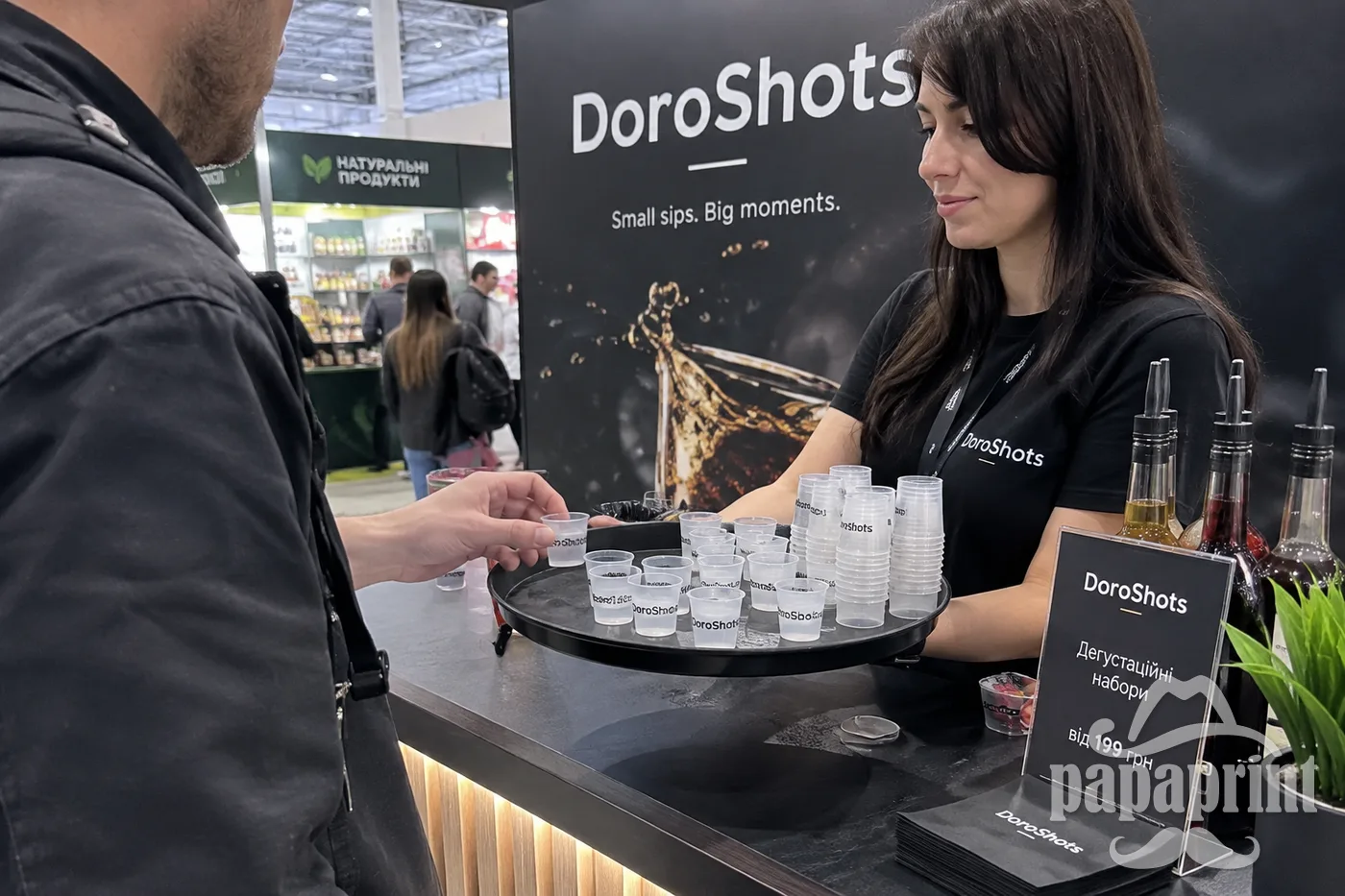 Брендовані шот-чарки DoroShots на дегустаційному підносі біля стенда виставки.