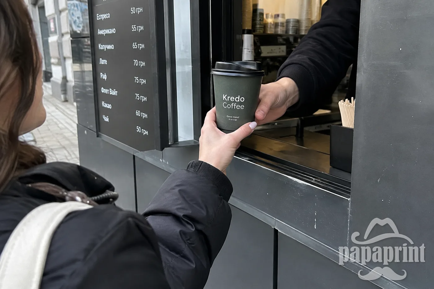 Біля вікна видачі Kredo Coffee клієнт отримує двошаровий стаканчик із кришкою через сервірувальний отвір.