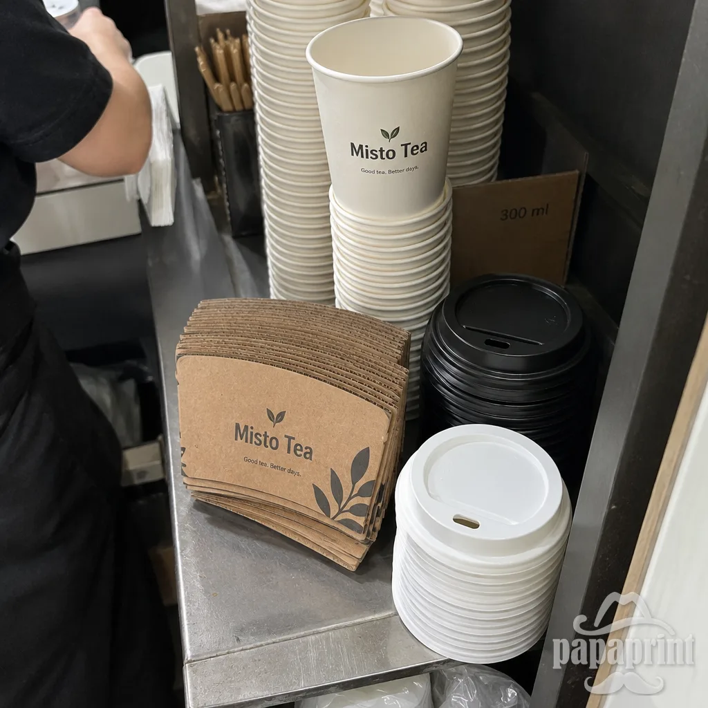 Крупний кадр згори: стопка капхолдерів Misto Tea лежить поруч зі стаканчиками на полиці кіоску в ТРЦ.