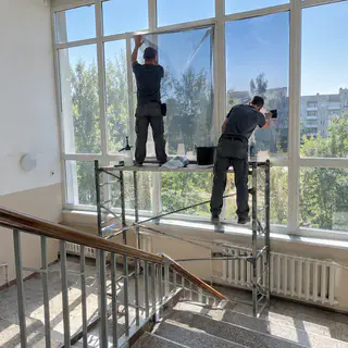 Монтажники клеять плівку на скляну стіну шкільних сходів зсередини (ілюстрація)
