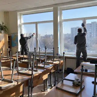 Монтажники клеять плівку на вікна класу під час канікул (ілюстрація)