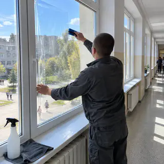Монтажник притискає плівку ракелем на вікні шкільного коридору зсередини (ілюстрація)